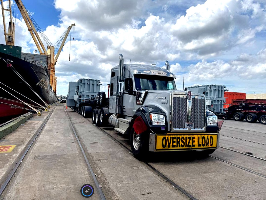 Kenworth heavy haul tractor with oversize load banner hauling transformers at a port terminal